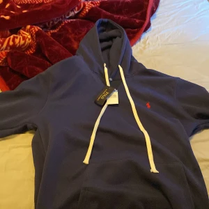 Blå hoodie från Ralph Lauren - Säljer en snygg blå hoodie från Ralph Lauren med det klassiska röda logotyp vid sidan. Hoodien har en justerbar dragsko i vitt och en stor ficka framtill. Perfekt för en avslappnad stil. Den är helt oanvänd ny pris 2125 mitt pris 700. Strl xxl.