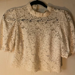 Vit spetsblus - Säljer en elegant vit spetsblus med trekvartsärm och hög krage. Blusen har ett vackert blommigt mönster och är perfekt för en stilfull look. Passar bra till både jeans och kjol.