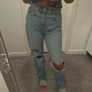 Ljusa jeans med slitningar - Snygga ljusa jeans med hög midja och slitningar på knäna. Perfekta för en avslappnad stil. De har en klassisk femficksdesign och en knappgylf.