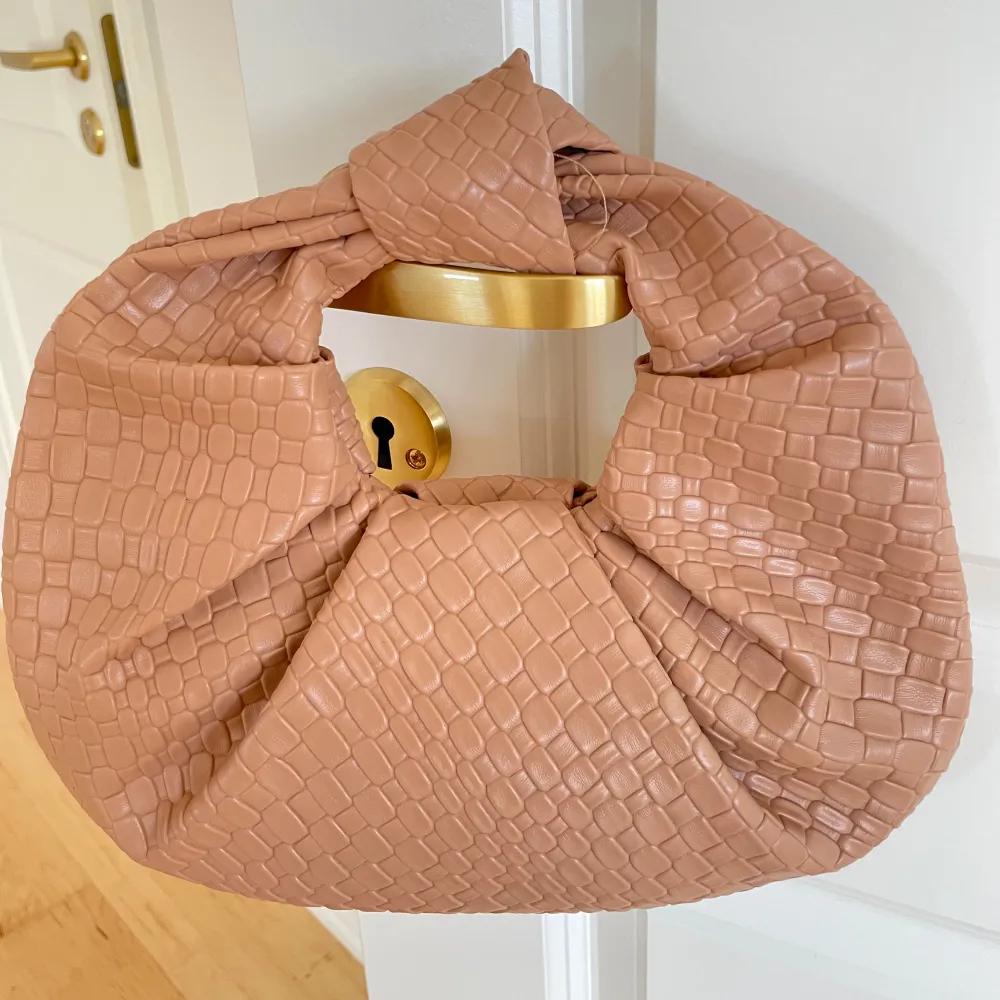 Snygg beige handväska med ett coolt krokodilmönster. Väskan har en unik knutdesign och är perfekt för att ge din outfit en trendig touch. Den är lätt att bära och passar till många olika stilar.. Laukut & Käsilaukut.