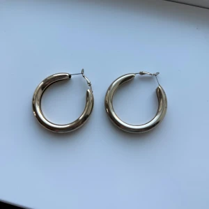 Guldfärgade hoop-örhängen - Snygga guldfärgade hoop-örhängen med en klassisk rund form. Perfekta för att ge en stilren touch till din outfit. De har en enkel stängning som gör dem lätta att bära.