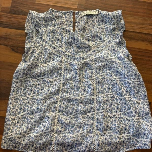 Blommig blus från Abercrombie & Fitch - Säljer en söt blommig blus från Abercrombie & Fitch i blått och vitt. Blusen har korta ärmar och fina spetsdetaljer. Perfekt för en somrig look!