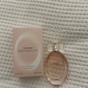 Calvin Klein Sheer Beauty Parfym - Calvin Klein Sheer Beauty är en elegant parfym i en stilren, oval flaska med en transparent kork. Doften är lätt och fräsch, perfekt för den som vill ha en subtil men ändå sofistikerad doft. Flaskan rymmer 50 ml och kommer i en ljusrosa kartong.