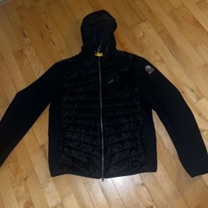 Parajumper cardigan - Säljer en svart jacka med huva och dragkedja. Jackan har en quiltad framsida och en patch på ärmen. Perfekt för kyligare dagar.                              Nypris:4499.                                                                     Pris kan diskuteras vid snabbaffär!