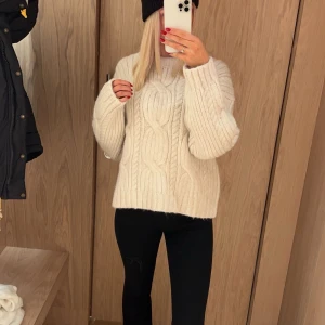 Vit stickad tröja - Säljer en mysig vit stickad tröja med kabelstickat mönster. Tröjan har långa ärmar och en avslappnad passform, perfekt för kyliga dagar. Den är både stilren och bekväm, ett måste i garderoben! 🧶