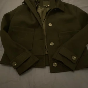 Svart kappa från lager 157 - Snygg svart kavaj från H&M med knappar framtill och på ärmsluten. Den har en klassisk krage och två stora fickor. Perfekt för en stilren look.