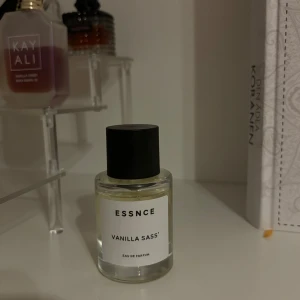 ESSNCE Vanilla Sass Eau de Parfum - En elegant flaska med ESSNCE Vanilla Sass Eau de Parfum. Doften har en söt och varm vaniljton, perfekt för den som älskar en mjuk och inbjudande doft. Flaskan är stilren med en svart kork och en enkel etikett. Låda finns kvar.