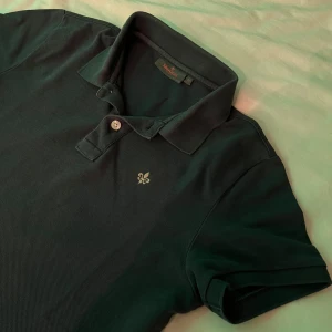 Mörkblå pikétröja från Morris - Säljer en stilren mörkblå pikétröja från Morris med klassisk krage och två knappar. Tröjan har en broderad detalj på bröstet och är kortärmad. Perfekt för en avslappnad men ändå snygg look. Nypris 999, säljer denna för 499/ halv pris. hör av dig vid minsta lilla fundering😉