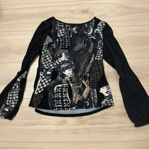 Svart långärmad topp med konstnärligt mönster - Unik svart topp med ett konstnärligt mönster i olika nyanser av brunt och beige. Toppen har långa ärmar och en rund halsringning. Perfekt för dig som vill ha något annorlunda i garderoben.