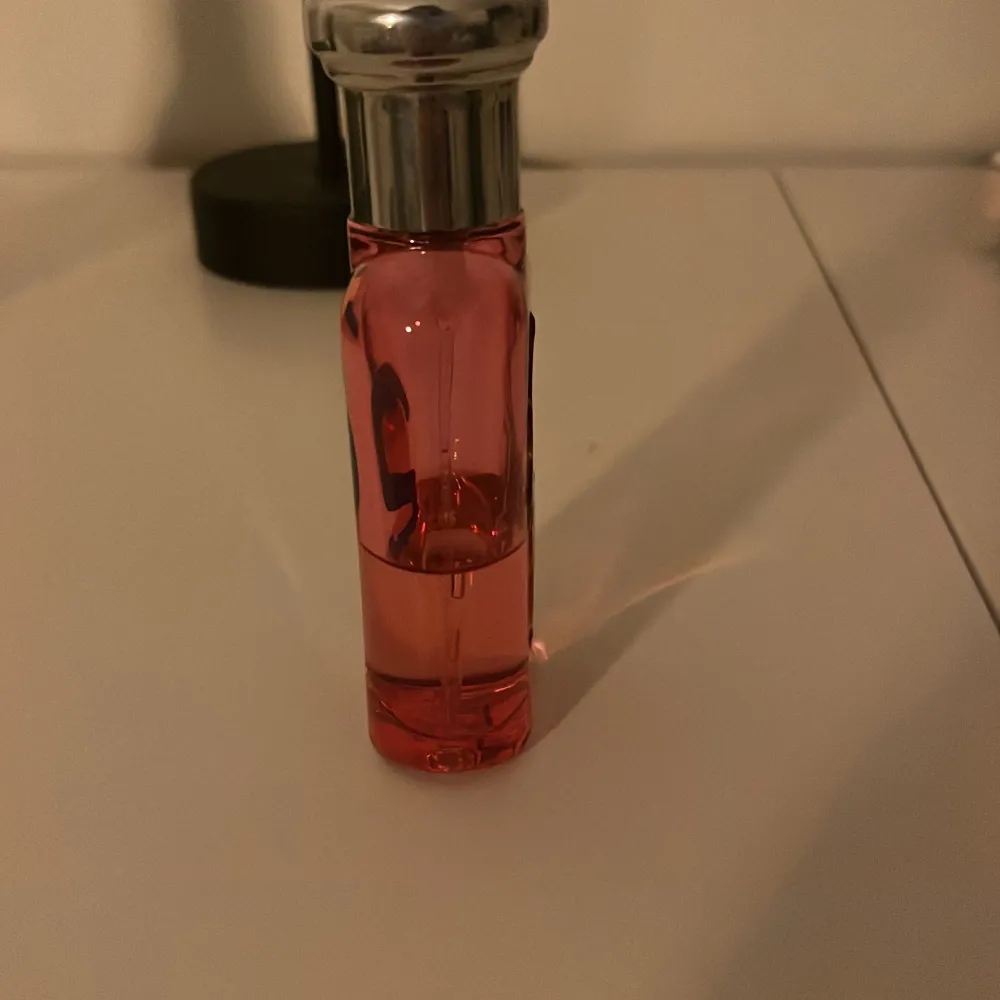 Säljer en rosa parfymflaska från Ralph Lauren med en grön polospelare och en stor blå siffra 2 på framsidan. Flaskan har en silverfärgad kork och en elegant design. Perfekt för den som gillar en sportig och stilren look. Halv full. Perfume.