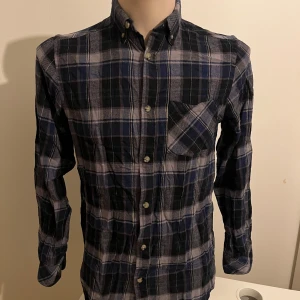 Rutig skjorta från EP Collection - Snygg rutig skjorta från EP Collection i blått och grått. Skjortan har långa ärmar och knappar framtill samt en bröstficka. Skön flanell perfekt för en avslappnad stil.