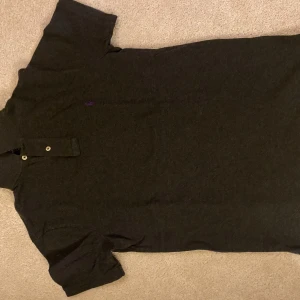 Mörkgrå pikétröja från Ralph Lauren - Säljer en stilren mörkgrå pikétröja från Ralph Lauren i slim fit. Tröjan har korta ärmar och en klassisk krage med knappar. Perfekt för en avslappnad men ändå elegant look.