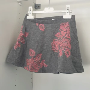 Grå kjol med rosa blommönster från L.O.G.G. - Säljer en söt grå kjol från L.O.G.G. med ett vackert rosa blommönster. Kjolen har en kort längd och är perfekt för en trendig look. Den är tillverkad i ett mjukt material som ger en bekväm passform.