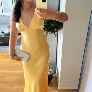 Gul långklänning med öppen rygg - Elegant gul långklänning med djup v-ringning och öppen rygg. Klänningen har en smickrande passform och är perfekt för speciella tillfällen. Tillverkad i ett mjukt och glänsande material som ger en lyxig känsla. Använd en gång! Klänningen har blivit lite nopprig på vissa ställen💛💛💛