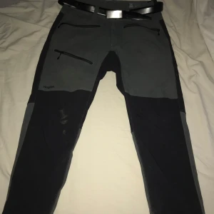 Svarta och grå byxor från Haglöfs - Säljer ett par svarta och grå byxor från Haglöfs i damstorlek 44. Byxorna har dragkedjor och är perfekta för utomhusaktiviteter. De är i mycket bra skick och har en praktisk design med flera fickor.