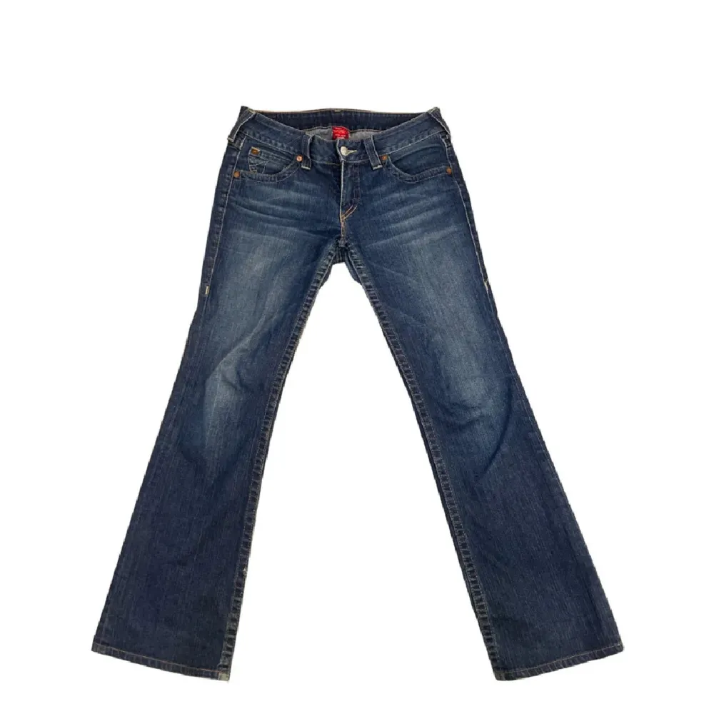 Säljer ett par snygga blå jeans från True Religion. De har en klassisk femficksdesign med coola detaljer på bakfickorna. Jeansen är i bootcut-stil och har en låg midja. Perfekta för en avslappnad look! 41 rakt över i midjan, 78 innerben och 101 ytterben. Jeans & Byxor.