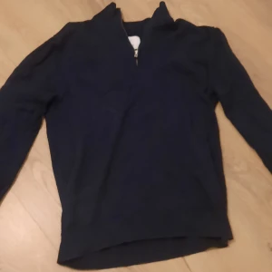 Mörkblå tröja med dragkedja från Bläck - Säljer en stilren mörkblå tröja med dragkedja i kragen. Perfekt för kyliga dagar och passar både till vardags och lite finare tillfällen. Tröjan har långa ärmar och är i bra skick. Skön och enkel att matcha med andra plagg.