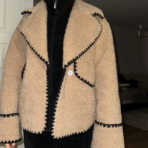  teddyjacka från Nelly  - Säljer en supermysig beige teddyjacka med svarta kantdetaljer. 