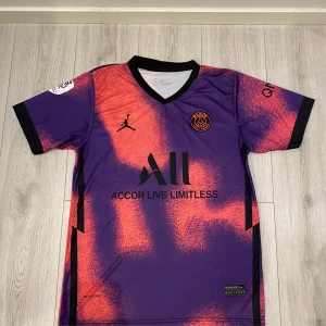 PSG Fotbollströja med Messi 30 - Säljer en PSG fotbollströja i lila och orange med Messi 30 på ryggen. Tröjan har korta ärmar och är i mycket bra skick. Perfekt för alla fotbollsfans som älskar unika och färgglada tröjor. Storlek L men passar även M 