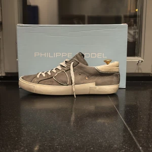 Grå sneakers från Philippe Model - Säljer ett par grå Philippe Model sneakers i bra skick. De har en snygg och stilren design med vita snören och en robust sula. Perfekta för både vardag och festliga tillfällen. Skorna är bekväma och passar bra till olika outfits. Nypris ligger på ca 3900kr men mitt pris ligger på endast 1499kr😮‍💨Fint skick skulle säga 6/10 enda defekterna är ett hål i innerskon vid hälen och ett av snörena (inget som syns när man använder skon!) Kan gå ner i pris vid snabb affär så tveka inte på att höra av er!☺️