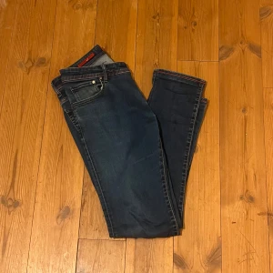 Mörkblå jeans från Jacob Cohen - Säljer ett par snygga mörkblå jeans från Jacob Cohen, modell Type 622. De har en klassisk femficksdesign med knappar och en unik broderad text på insidan. Perfekta för både vardag och fest!