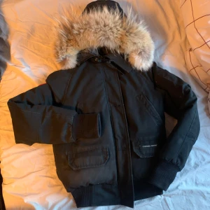 Svart dunjacka från Canada Goose - Säljer en svart Canada Goose dunjacka i bra skick förutom några slitningar som syns på sista bilden. Den har en fluffig pälsfodrad huva och ribbade muddar. Perfekt för kalla vinterdagar. Jackan har en dragkedja och flera praktiska fickor. 