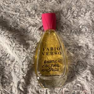 Säljer en flaska Fabio Verso Exotic Cocktail Eau de Parfum. Den har en elegant, droppformad flaska med en klar gul vätska och en snygg rosa kork. Perfekt för dig som älskar exotiska dofter! 🌺