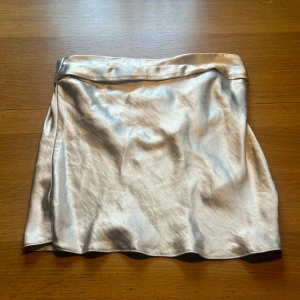 Krämfärgad satin topp - Snygg krämfärgad topp i satin med en elegant glansig yta. Perfekt för festliga tillfällen eller en utekväll. Toppen har en stilren design med en elastisk midja för bekväm passform. Helt ny med tag kvar!