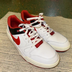 Nike Full Force vitt och rött - Säljer ett par snygga Nike Full Force i vitt med röda och svarta detaljer. Använt endast en gång då dom inte passade mig och glömde lämna tillbaka dom. Har tyvärr inte lådan kvar efter jag flyttade men köptes från Nike och kan visas i appen som ”kvitto”. Skriv vid flera frågor!