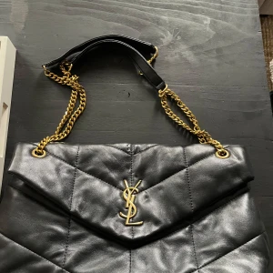 Svart quiltad axelväska - Snygg svart quiltad axelväska med guldkedjor och ett elegant YSL-emblem på framsidan. Perfekt för både vardag och fest! 🖤OBS! Går EJ ner i pris! Det är redan ett jättebra pris! 