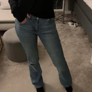 Blå jeans med slitning - Säljer ett par snygga blå jeans i bra skick. De har en cool slitning på ena knät och en straight passform som ger en avslappnad look. Perfekta för vardagsbruk och kan enkelt matchas med olika toppar. Passar bra till både sneakers och boots.