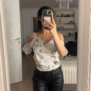 Vit blommig offshoulder topp - Säljer en söt vit offshoulder topp med blommigt mönster. Toppen har korta ärmar och en luftig passform, perfekt för sommardagar. Den har en romantisk stil med volangdetaljer vid ärmarna. Passar bra till både jeans och kjol!