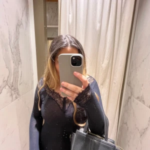 Svart långärmad topp med spetsdetaljer - Säljer en elegant svart långärmad topp med vackra spetsdetaljer vid halsringningen. Perfekt för en kväll ute eller en festlig tillställning. Toppen har en tight passform som framhäver figuren. Passar bra till både jeans och kjol. 🖤