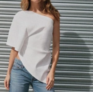 Vit oneshoulder topp - Snygg vit oneshoulder topp. Den har en asymmetrisk design med en ärm och en axel bar. Passar bra till både jeans och kjol för en stilren look. Skickar egna bilder på begäran 🤍