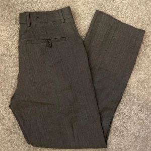 Grå kostymbyxor - Snygga grå kostymbyxor från Banana Republic i bra skick. De har en klassisk straight passform och är perfekta för både kontoret och finare tillfällen. Byxorna har knappar och hällor för bälte, vilket ger en stilren look. Materialet är ull och polyester och ser exklusivt ut. Perfekt för höst , vinter och vår!