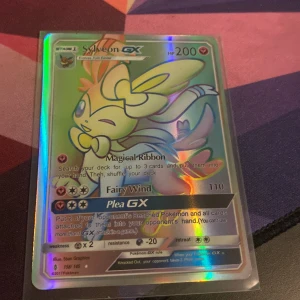 Sylveon GX Pokémonkort - Säljer ett Sylveon GX Pokémonkort. Kortet har en holografisk yta och visar Sylveon i en glad pose. Kortet är i bra skick och perfekt för samlare eller spelare som vill stärka sin lek. Ny pris 1,000 på ebay.