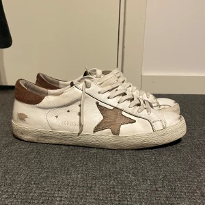 Golden Goose Skor - Säljer ett par vita Golden Goose med brun stjärna. De har en vintage look med slitna detaljer och brunt mocka på hälen. Perfekta för en avslappnad stil! Skorna har snörning och är i bra skick 7,5/10. storlek 41 passar 42,5! fler frågor eller funderingar hör av er!🙌