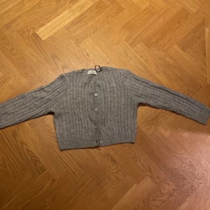 Grå stickad kofta från H&M - Säljer en supermysig grå stickad kofta från H&M. Den har ett klassiskt flätmönster och knappar framtill. Perfekt för kyliga dagar och passar både till vardags och lite finare tillfällen. 🧶✨