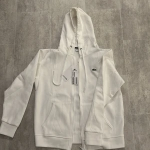 Vit hoodie och byxor från Lacoste - Säljer en snygg tracksuit som är helt ny. Tracksuiten är i bra skick då jag inte använt den. Jag fick den i födelsedagspresent av mina föräldrar, men den passade inte och jag har inget kvitto då mina föräldrar inte sparade det. Säljer för 1750, men pris är inte hugget i sten. Storlek M kom privat för mer frågor.