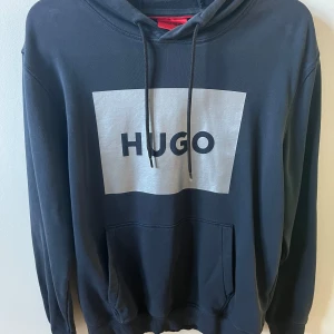Hugo hoodie - En mörkblå Hugo hoodie med stort silvrigt tryck på bröstet. Lite urtvättad, annars rätt så bra skick. Storlek M
