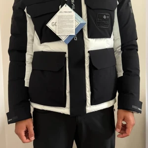 Sail racing glacier jacket - Säljer en snygg och varm dunjacka från Sail racing i svart och vitt. Jackan har en cool design med stora fickor och en huva. Perfekt för kalla vinterdagar. Den är i mycket bra skick då den aldrig är använd. Hojta till vid intresse. PS. Svarar ej på skambud.