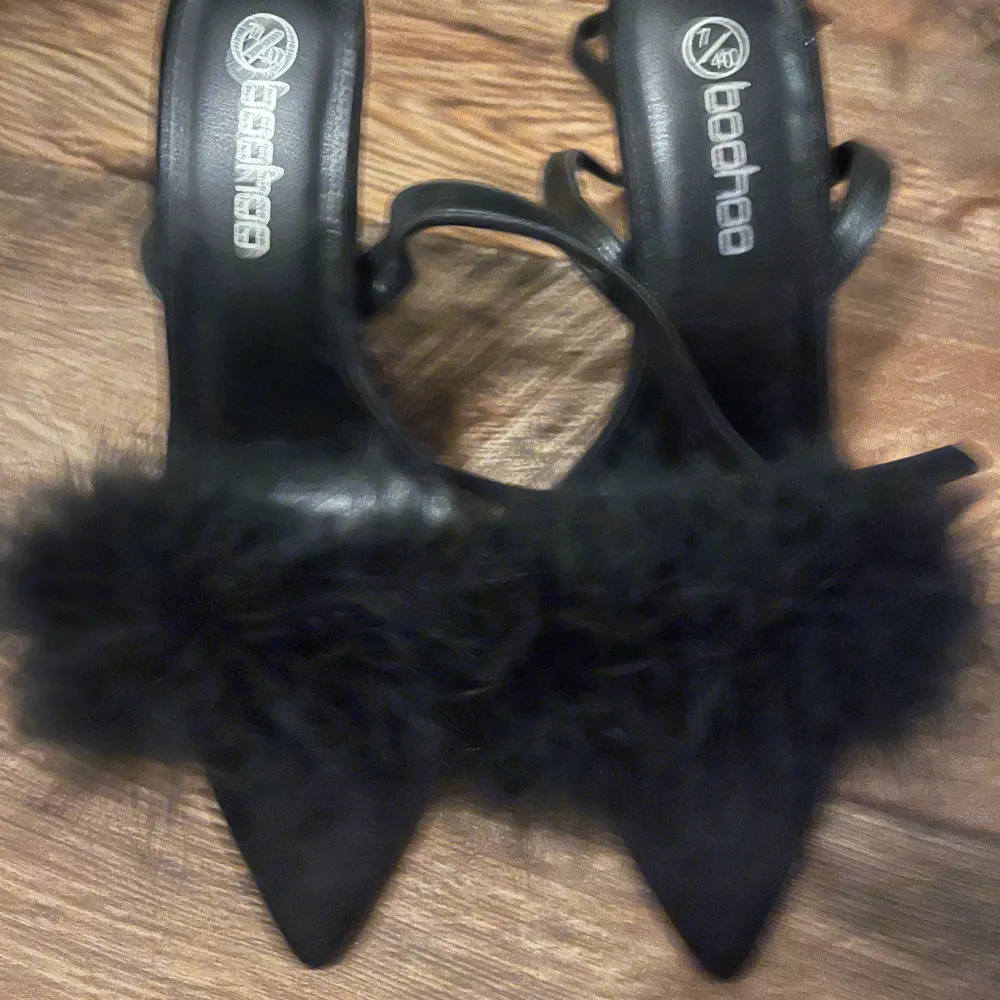 Snygga svarta klackskor från Boohoo med en fluffig pälsdetalj över foten. De har en spetsig tå och en elegant klack som passar perfekt för festliga tillfällen. Skorna är i bra skick och redo att användas för att ge din outfit en extra touch av glamour.. Kengät.