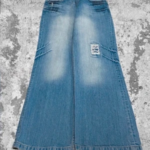 Blå jeans med slitningar - Säljer ett par coola blå jeansk med slitningar och en avslappnad look. Byxorna har en lång modell och är perfekt för en casual stil. Den har fickor både fram och bak, vilket är superpraktiskt. Passar perfekt till sneakers eller boots för en avslappnad vibe.   Midja: 80cm.     Total längd: 107cm.  Ben: 26 cm