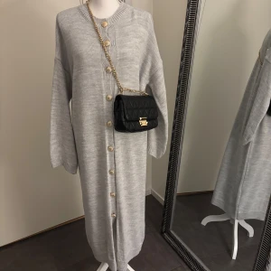 Knitwear Golden Button Dress | Gray - Hej! Detta är mitt företag, och du kan köpa produkten här på plick eller via vår hemsida: Nooralanna.com. Det pris som anges är fast, och jag kommer inte att svara på meddelanden om budgivning. Tack för förståelsen! 	•	Färg: Grå 	•	Längd: 133 cm       •     Kan öppnas och ha som cardigan  	•	Lagerstatus: 2 st kvar  Retur gäller endast via beställning på hemsidan. Läs retur policy vad som gäller.   Kontakta mig gärna vid seriösa frågor eller köp. Tack!