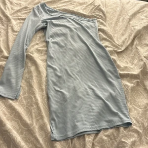 Ljusblå oneshoulder klänning - Säljer en superfin ljusblå oneshoulder klänning i ribbat material. Perfekt för både vardag och fest! Klänningen har en tight passform och är i mycket bra skick. Den är bekväm och stilren, perfekt för vår och sommar.