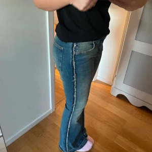 Blå jeans med fransdetaljer - Säljer ett par snygga blå jeans med fransdetaljer längs sidorna. De har en klassisk femficksdesign och en bekväm passform. Perfekta för en avslappnad vardagslook! 🦋