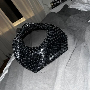Svart flätad väska - Säljer en superfin svart flätad väska i syntetmaterial. Den har en unik design med ett runt handtag och en dragkedja för säker förvaring. Perfekt för både vardag och fest! 🖤