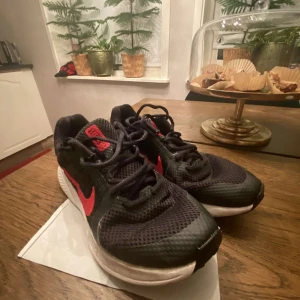 Svarta Nike löparskor  - Säljer ett par svarta Nike sneakers med röda detaljer. De har en snygg och sportig design med snörning och en bekväm sula. Perfekta för både träning och vardagsbruk. Skorna är i bra skick och redo för nya äventyr!