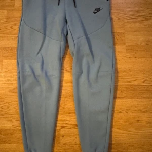 Ljusblå  mjukisbyxor från Nike - Säljer ett par ljusblå/marinblå mjukisbyxor från Nike i mycket bra skick. De har en bra passform och är perfekta för träning eller en chill dag hemma. Byxorna har dragkedjor vid fickorna och en snygg Nike-logga på ena benet. Superbekväma och stilrena!