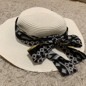 Vit solhatt med avtagbara band - Snygg vit solhatt perfekt för sommardagar! Hatten har en bred brätte och kommer med två avtagbara band: ett svartvitt mönstrat och ett blåvitt randigt. Banden kan knytas i en rosett för extra stil. Perfekt för stranden eller en dag i parken!